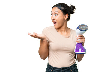 Wall Mural - Young Uruguayan woman holding a vertical steam iron over isolated chroma key background with surprise facial expression