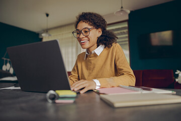 Wall Mural - Smiling female manager working remotely on laptop from home while sitting at living room