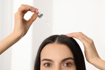 Poster - Woman applying hair serum in room, closeup. Cosmetic product