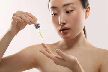 Wall Mural - Beautiful young woman applying cosmetic serum onto her finger on white background, selective focus