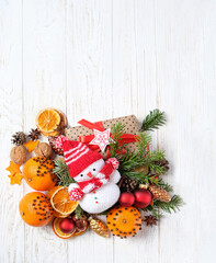 Wall Mural - Christmas background. knitted snowman toy, Gift box, fir branches, oranges decorated cloves on wooden table. Christmas, New Year holidays concept. festive winter season. top view. copy space