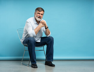 Wall Mural - Portrait of a casual senior sitting on a chair on blue background