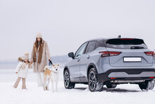 Woman With Her Daughter And Dog Having A Walk In A Snowy Park By Their Car