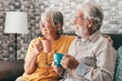 Happy mature 50s husband and wife sit rest on comfortable sofa in living room enjoy tea talking, smiling elderly 60s couple relax on couch at home drink coffee chat speak laugh on leisure weekend.