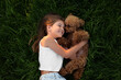 Beautiful girl with cute Maltipoo dog on green lawn outdoors, top view