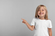 Special promotion. Smiling girl pointing at something on grey background. Space for text