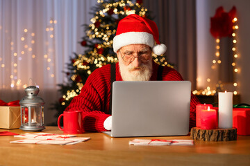 Canvas Print - Santa Claus using laptop at his workplace in room with Christmas tree