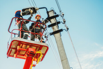 Two electricians from cradle of aerial platform or crane are repairing street lighting lamp. Professional electricians wearing helmets, overalls and insurance work at heights. View of workers from