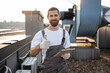 © sofiko14 - Serious construction worker in overalls and gloves standing and using modern tablet outdoors. Caucasian professional man surfing internet while working with devices on roof of factory.