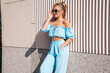 © halayalex - Young beautiful smiling hipster woman in trendy summer clothes. Sexy carefree woman posing in the street at sunset. Positive blond model outdoors. Cheerful and happy. Near wall. In sunglasses