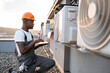 © sofiko14 - Side view of skilled man typing on wireless laptop while kneeling near hanging air conditioner outdoors. African american specialist using modern technologies for quickly repairing of cooling system.