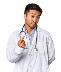 Wall Mural - Young Chinese man as a medical doctor in studio pointing with finger at you as if inviting come closer.