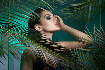Wall Mural - Beauty tropical portrait of a woman in palm leaves, wet long hair, green eye shadow makeup