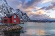 Typical Lofoten red rorbuer house with wooden pier at sunset with snowcapped mountains