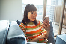 Smiling happy woman holding smartphone on home sofa