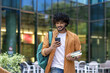 © Tetiana - Indian young male student walking on street near campus and university with backpack. Holds books and uses a mobile phone