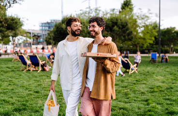 Happy young men couple walking along lawn in park