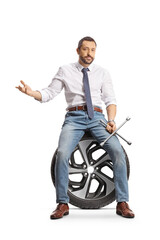 Poster - Serious man sitting on a car tire and holding a lug wrench