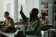 © pressmaster - African American guy in military uniform and eyeglasses raising hand and looking at teacher after lecture or presentation to ask question