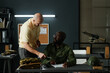 © pressmaster - Young African American man looking at mature teacher of military training while both pointing at his notes during discussion of new subject