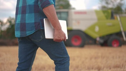 Wall Mural - farmer in a wheat field. agricultural business concept. An experienced farmer walks through wheat field with a tablet in his hands next to combines. farmer working in the field with wheat sprouts