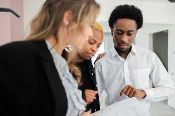 Blonde young woman estate agent provided the black african american homeowners with a market analysis to determine the optimal sale price for their property.