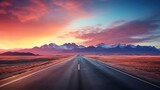 Fototapeta Niebo -  a long stretch of road in the middle of a desert with a mountain range in the background and a pink and blue sky with a few clouds in the foreground.