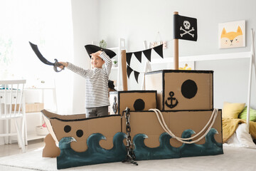 Wall Mural - Cute little pirate playing with sword in cardboard ship at home