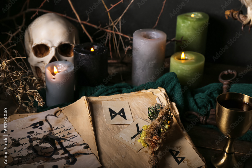 Witch's magic attributes with burning candles, book and dry flowers on dark table, closeup