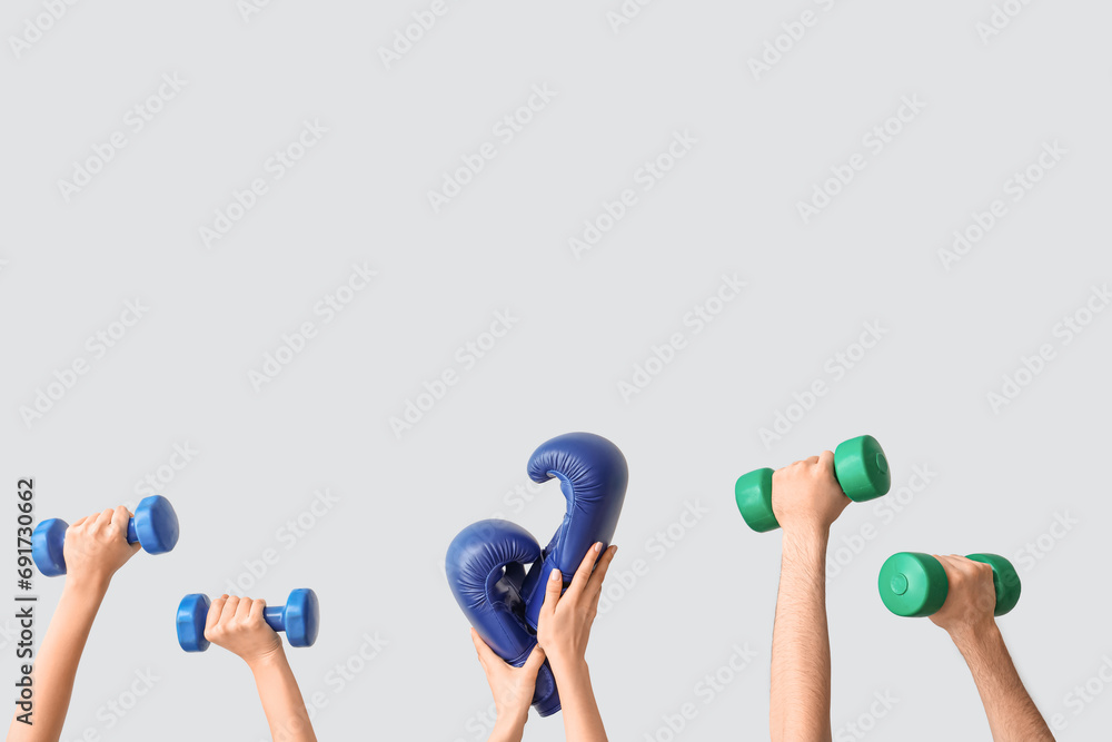 Female hands with dumbbells and boxing gloves on grey background