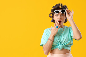 Poster - Shocked young woman with hair curlers on yellow background