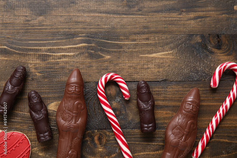 Composition with chocolate Santa Clauses and candy canes on wooden background