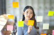 © David - Happy asian businesswoman planning new project with sticky note in a creative writing on blank office glass