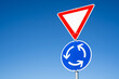 Triangular warning sign and blue round sign with arrows on a roundabout road