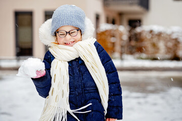 Wall Mural - Portrait of adorable little girl outdoors on cold winter day. Cute preschool child in warm clothes, with knitted hat and scarf. Happy girl with eyeglasses having fun with snow.