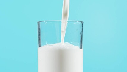 Wall Mural - Slow motion of milk drink pouring into glass on blue background