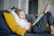 © evgeniia_1010 - At home, a charming girl with blonde hair is sitting on the couch, and she is reading an exciting book.