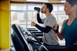Athletic man drinks water while working out on treadmill in gym.