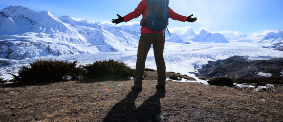 Wall Mural - Woman hiker enjoy the view on mountain top cliff edge face to glacier mountains