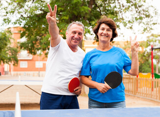 Mature couple showing victory near table tennis