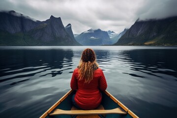 Wall Mural -  a woman in a red jacket is sitting in a boat in the middle of a lake with mountains in the background.