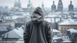 Back view of an unrecognizable lonely man in a hood standing against the backdrop of a snowy city outdoors