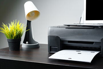 Modern printer with paper and laptop on table in office