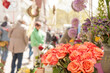 Orangefarbener Rosenstrauß an Marktstand vor unscharfen Marktbesucherinnen