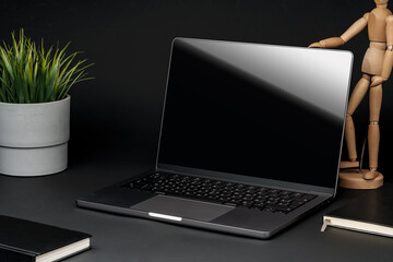 Canvas Print - Open laptop with wooden mannequin on table against black background