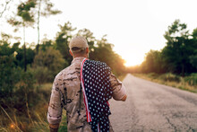 Back View Of Unrecognizable Mature Commando On Road With American Flag On Shoulder Under Sky During Sunset