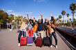 © Gigi Delgado - Group of middle aged friends posing for the camera happily celebrating their holidays. Diverse people with arms up and their luggage in the street on a sunny day.