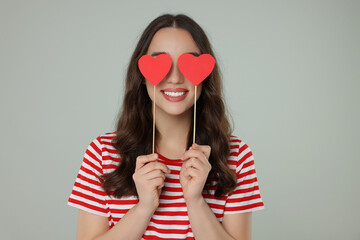 Wall Mural - Young woman covering her eyes with paper hearts on grey background