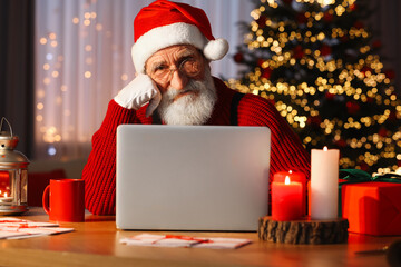 Canvas Print - Santa Claus using laptop at his workplace in room with Christmas tree