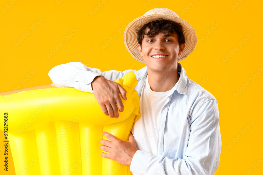 Young man with swim mattress on yellow background